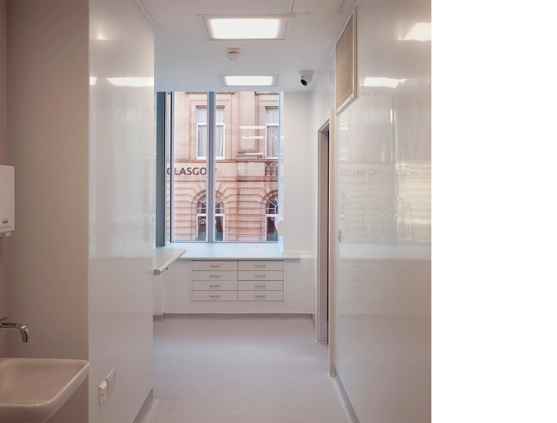 Operating room corner with large storage space finished all in minimalist white with large glass façade allowing natural light inside the medical premises.