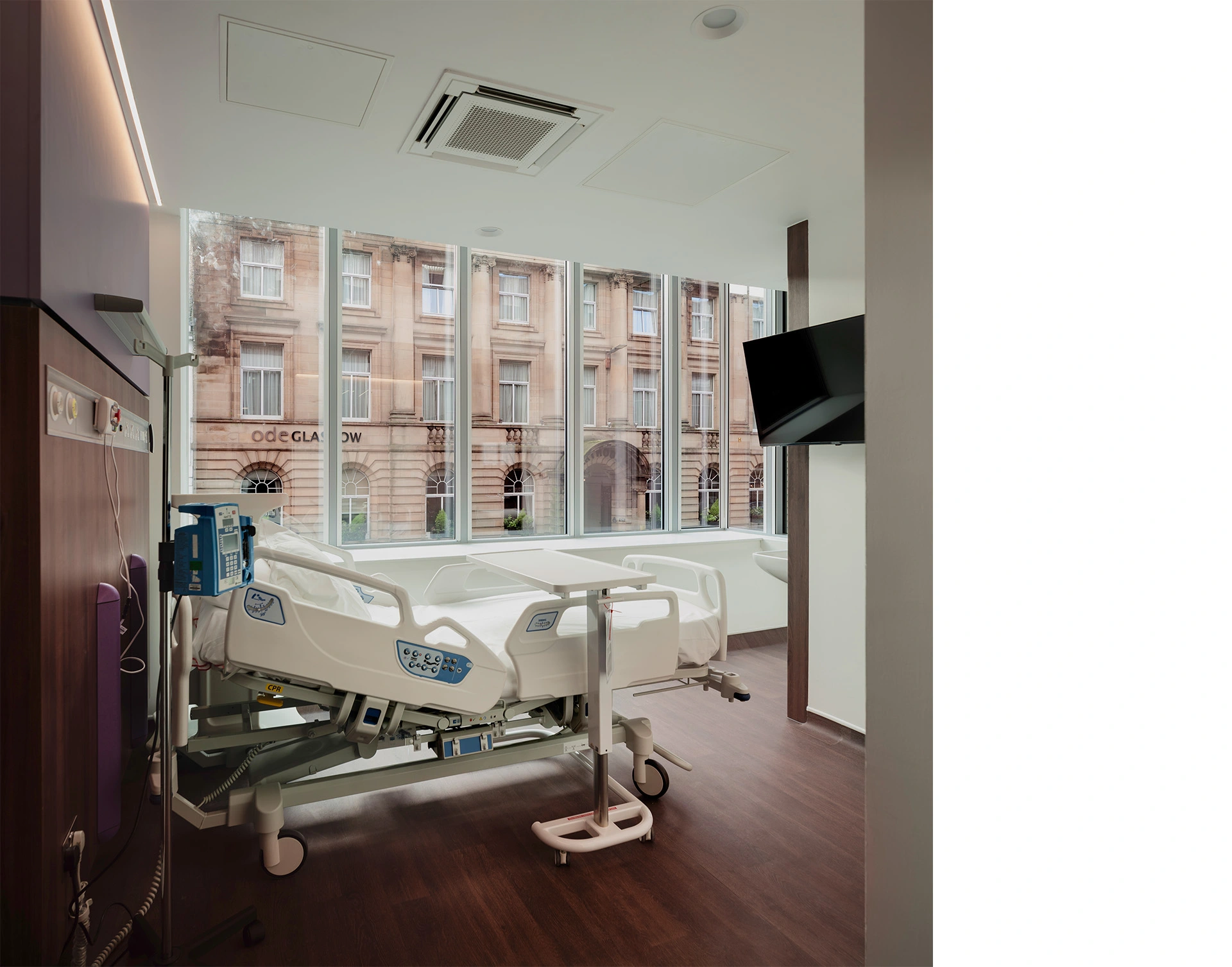 Recovery room view towards and across the tall glazing providing natural light and stunning views from inside towards Glasgow Bath Street, with dark timber vinyl flooring, and white ceiling and walls.