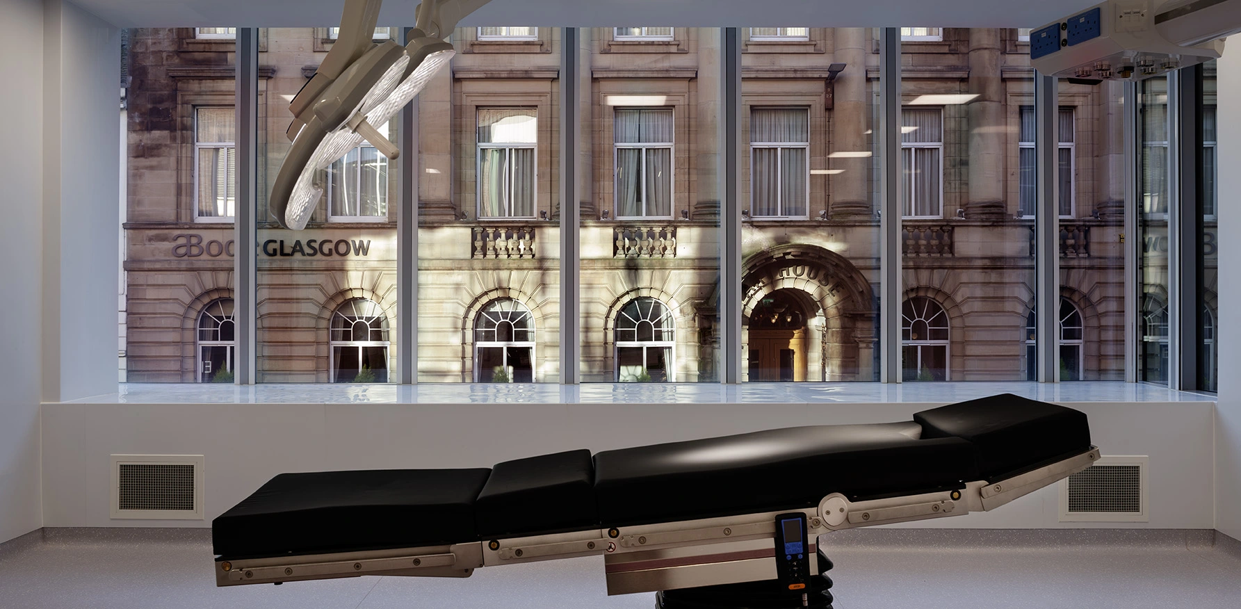 Recovery room view towards and across the tall glazing providing natural light and stunning views from inside towards Glasgow Bath Street, with dark timber vinyl flooring, and white ceiling and walls.