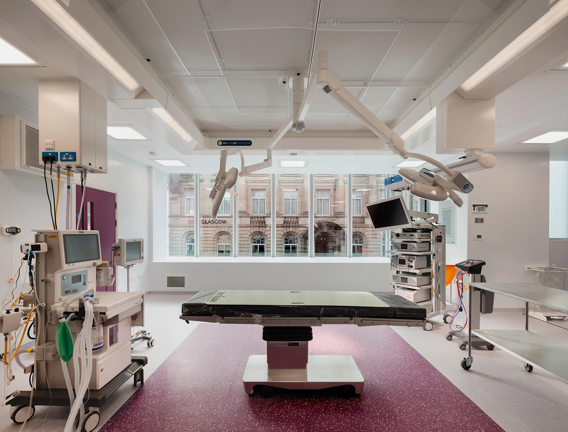 Large surgery room, with modern state-of-the-art equipment in the middle of Bath Street Glasgow, with large glass faced windows showcasing the gorgeous architecture of the buildings across the street. This specialised patient comfort and surgeon needs dream operating environment is designed by award-winning healthcare architects.