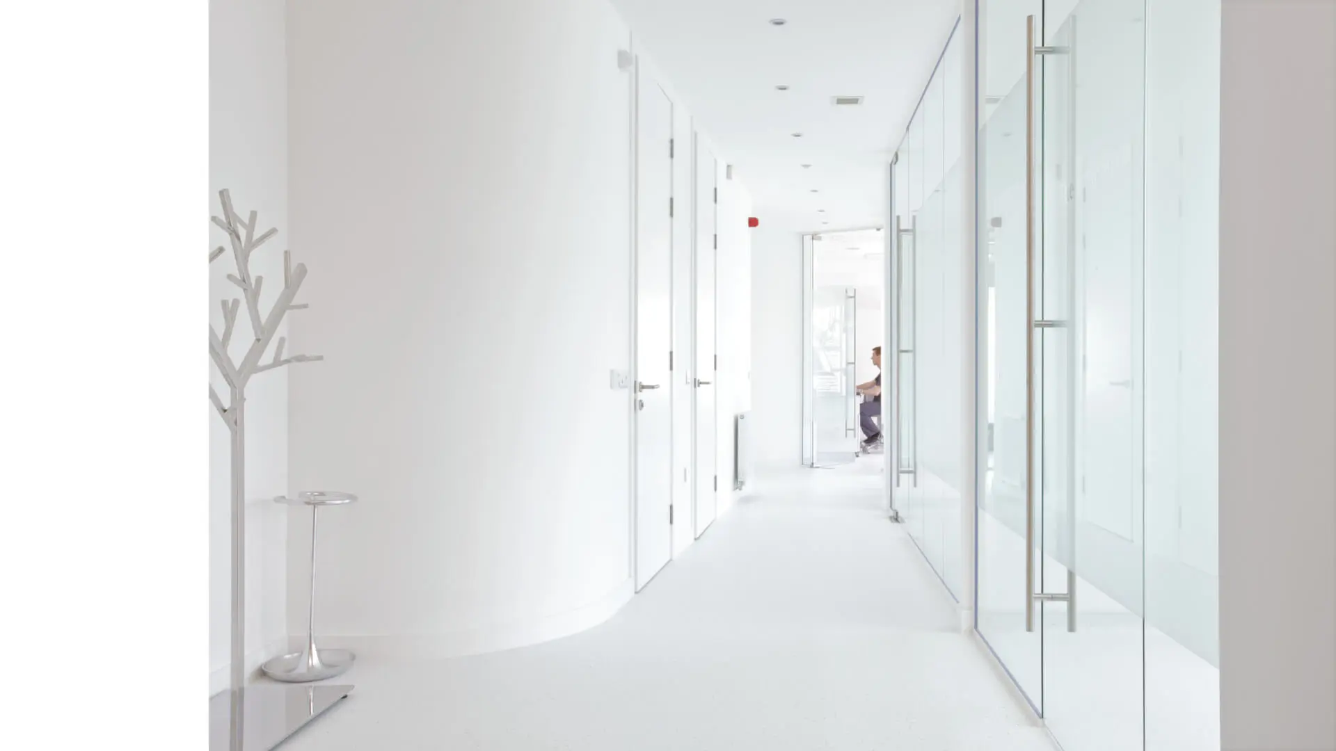 Bright and modern corridor of a dental practice with floor-to-ceiling glass partitions, designed by healthcare architects. The transparent medical facility design emphasizes cleanliness and openness, essential for healthcare environments. This dental design layout highlights efficient use of space, offering privacy while maintaining a welcoming atmosphere. This project was designed by NVDC healthcare and dental practice design specialists Glasgow in Edinburgh Scotland for an NHS facility.