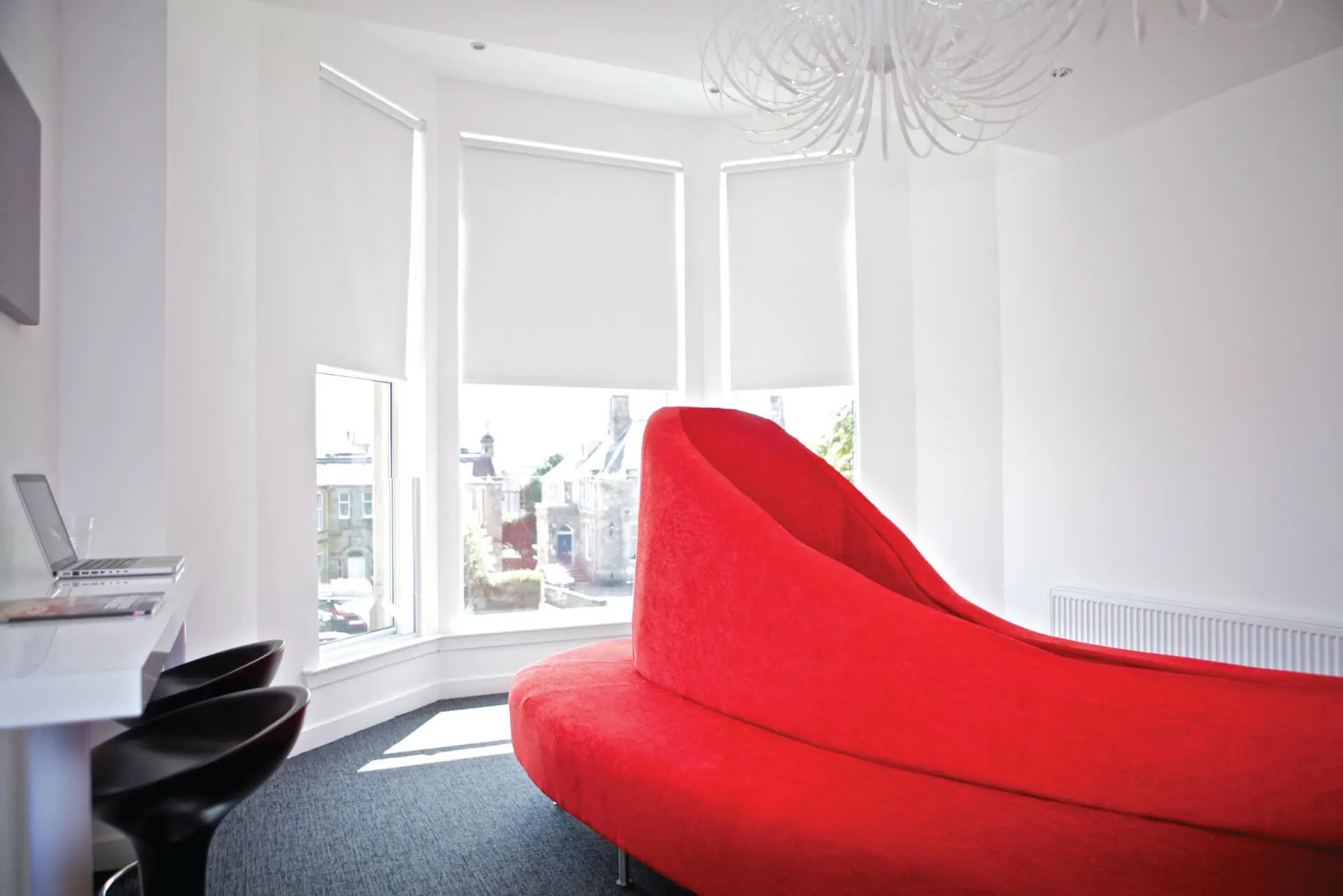 Open and airy dental practice with large windows and natural light, featuring a red statement seating area, minimalistic decor, and modern pendant lighting. Designed by a healthcare architect focused on modern and inviting dental practice design. This project was designed by NVDC healthcare and dental practice design specialists Glasgow.