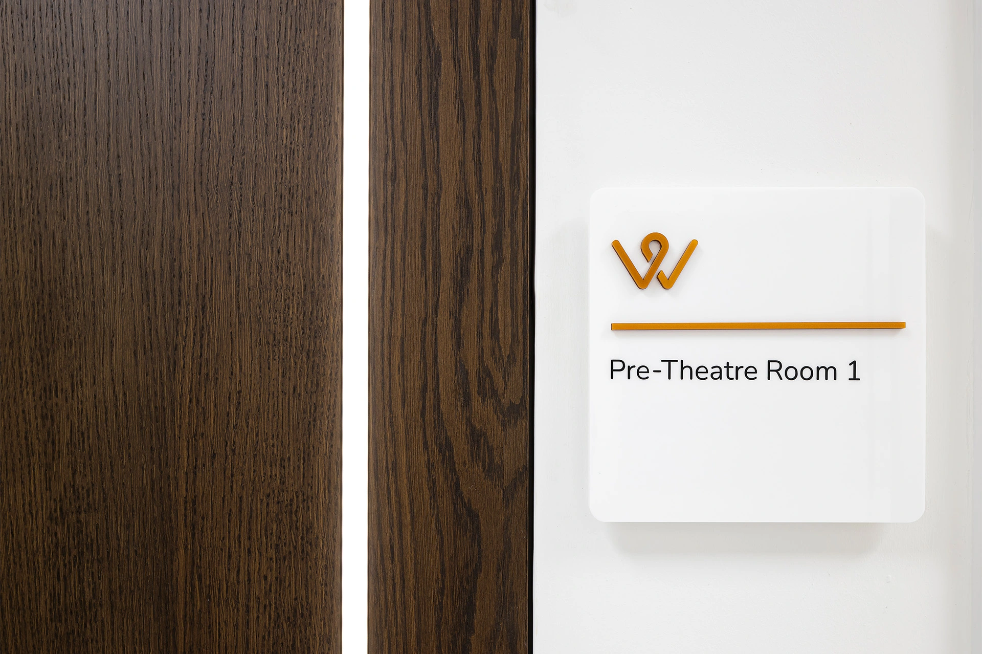 A signage on an operating surgery theatre, with a dark timber door visible next to it, with a long white matted strip showing light through to let the outside viewer know the theatre is in use.