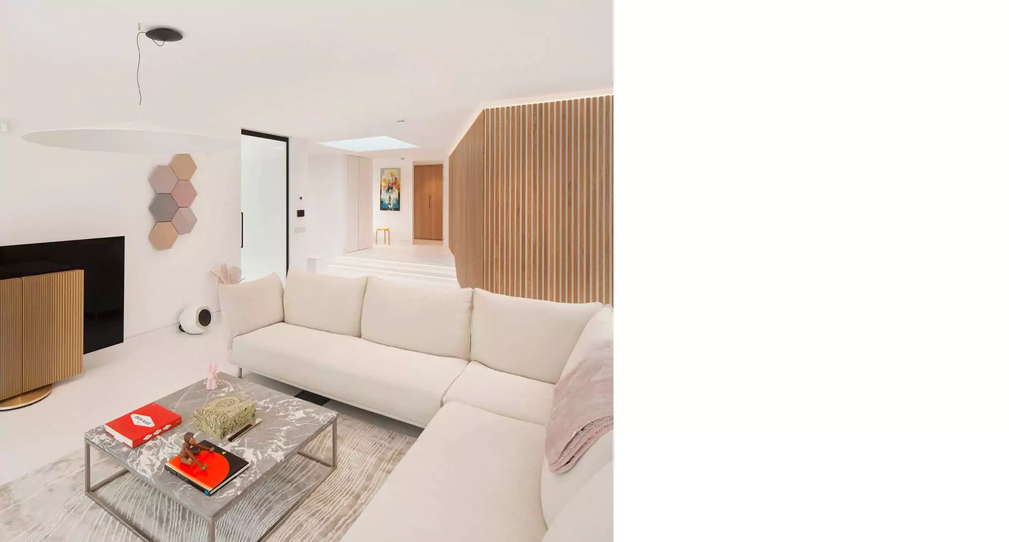 Elegant open-plan living area in a Glasgow home renovation project by leading architects, featuring minimalist interior design with clean lines, a neutral colour palette, and custom white furniture. This remodelling project highlights the use of innovative lighting and modern design elements to create a spacious and inviting environment, ideal for contemporary living. The space exemplifies architectural expertise in integrating functionality with aesthetic appeal. There are LEDs behind the timber batten wall and the two steps behind the entrance creating a floating effect. A large rooflight is visible above the entrance in the background providing good natural light inside the house.