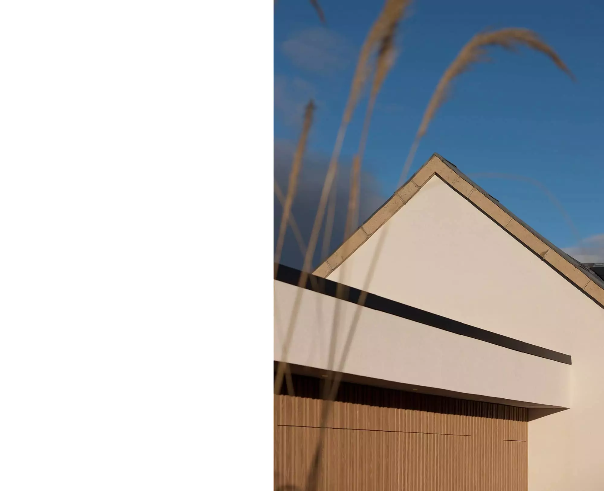 Contemporary house extension in Glasgow featuring a minimalist exterior design with white render, angled roofline, and zinc cladding. Designed by leading Glasgow architects specializing in home remodelling and renovation. The modern architecture emphasizes natural light through rooflights, enhancing the open-plan living space inside. there is a garage door showing in the foreground finished in timber batten panels with minimalist and luxurious detailing.
