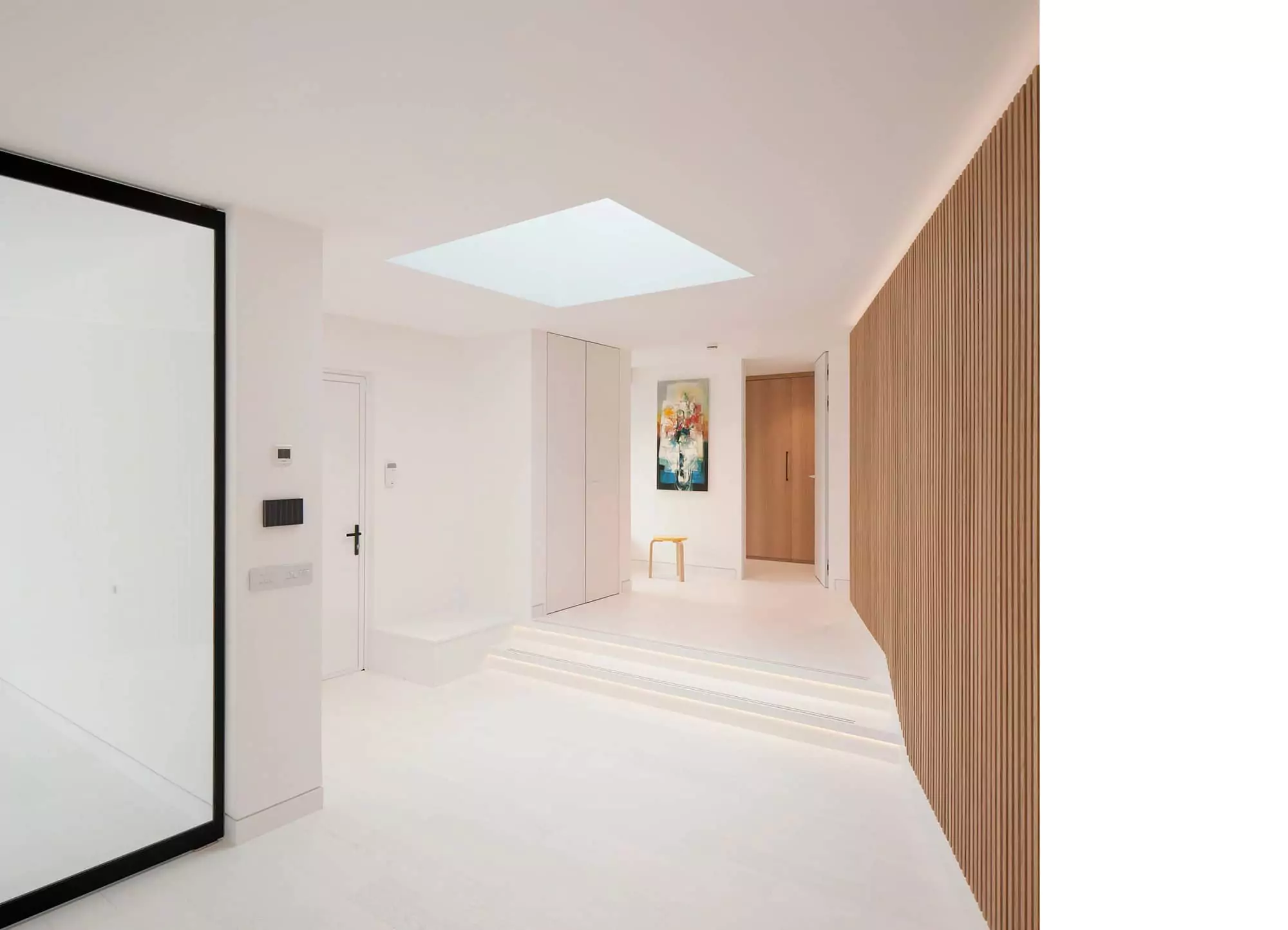 Contemporary entrance area of a home remodelling in Glasgow, featuring a large rooflight that bathes the space in natural light. The open-plan living area is complemented by white interiors, floor-to-ceiling wooden slats, and subtle LED lighting, all hallmarks of modern architectural design. This renovation and house extension project showcases the expertise of Glasgow architects in creating light-filled, airy spaces.