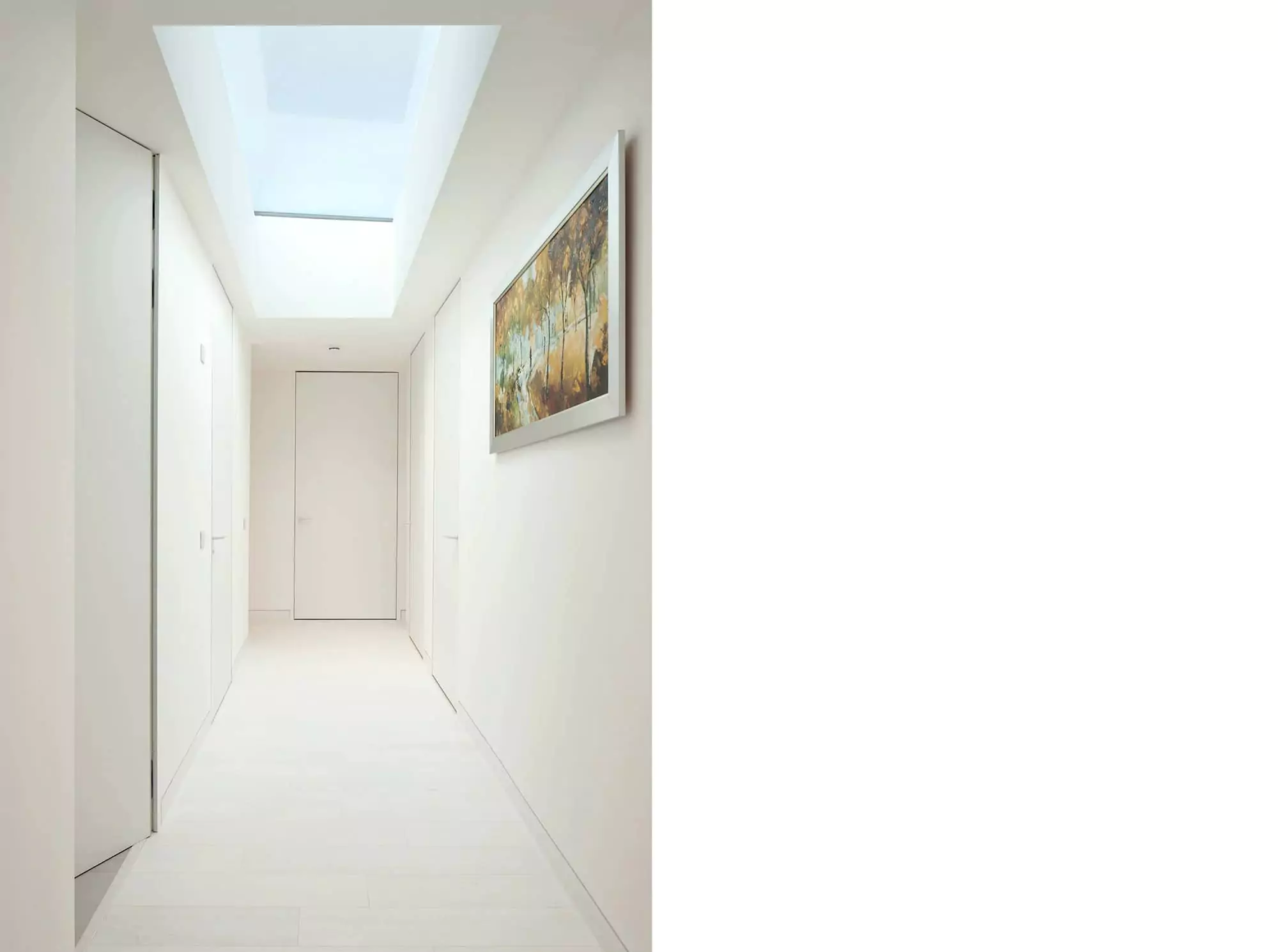 Bright hallway featuring a stunning rooflight that floods the space with natural light, showcasing the work of Glasgow architects in this modern house extension. The minimalist interior design, complemented by white walls and white hardwood floors, enhances the sense of openness and space. This renovation project highlights the seamless integration of contemporary elements in a home remodelling project.